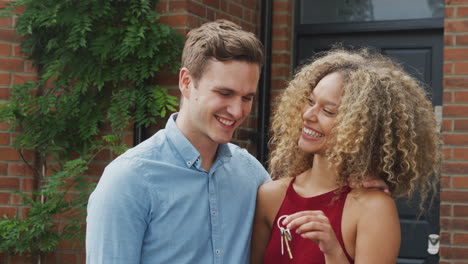 Portrait-Of-Excited-Young-Couple-Standing-Outside-New-Home-Holding-Keys-Together