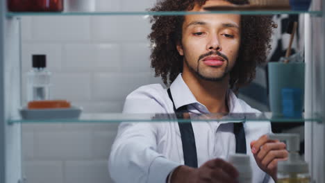 View-Through-Bathroom-Cabinet-Of-Young-Man-Taking-Medication-From-Container