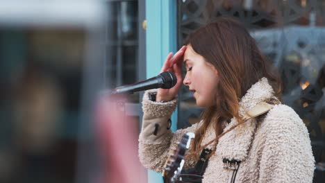 Person-Filming-Female-Musician-Busking-Playing-Acoustic-Guitar-And-Singing-To-Crowd-On-Mobile-Phone