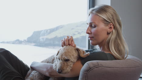Woman-Relaxing-In-Chair-By-Window-At-Home-With-Pet-Dog