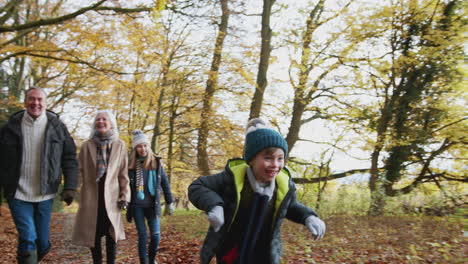 Multi-Generation-Family-Walks-Along-Path-Through-Autumn-Countryside-With-Boy-Running-Ahead