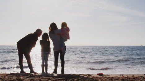 Rear-View-Of-Grandmother-With-Mother-And-Granddaughters-Looking-Out-To-Sea-Silhouetted-Against-Sun