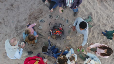 Drone-Shot-Of-Multi-Generation-Family-Toasting-Marshmallows-Around-Fire-On-Winter-Beach-Vacation