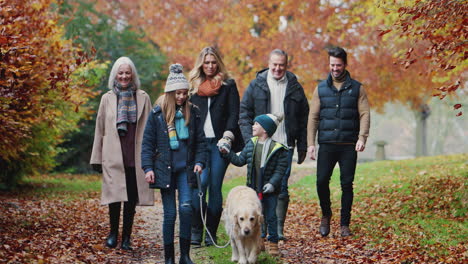 Lächelnde-Mehrgenerationenfamilie-Mit-Hund,-Die-Gemeinsam-Den-Weg-Durch-Die-Herbstliche-Landschaft-Entlang-Geht