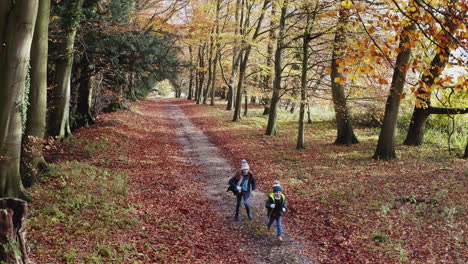 Drone-Shot-Of-Two-Children-Having-Fun-Running-Along-Path-Through-Autumn-Countryside-Together