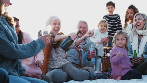 Mehrgenerationenfamilie-öffnet-Im-Winterstrandurlaub-Eine-Flasche-Und-Schenkt-Getränke-Ein