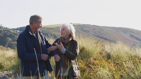 Loving-Active-Senior-Couple-Walking-Arm-In-Arm-Through-Countryside-Together