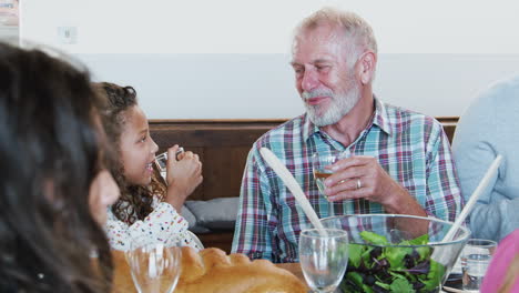Grandfather-And-Granddaughter-Making-A-Toast-As-Multi-Generation-Family-Meet-For-Meal-At-Home