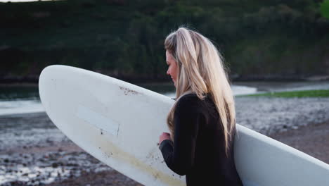 Woman-Wearing-Wetsuit-Walking-Along-Beach-Into-Sea-Holding-Surfboard-Enjoying-Surfing-Vacation