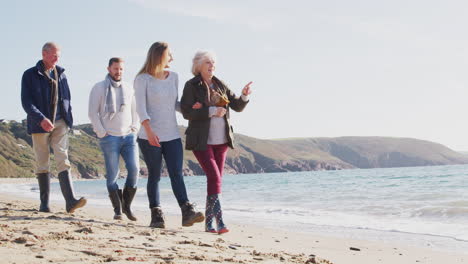Senior-Couple-Walking-Along-Shoreline-With-Adult-Offspring-On-Winter-Beach-Vacation