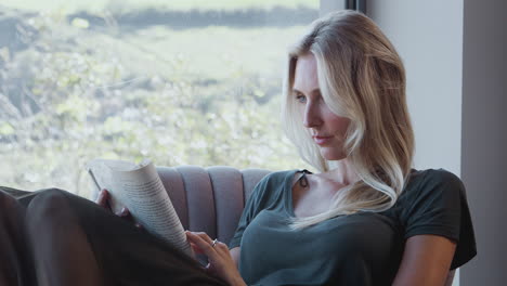 Woman-Relaxing-In-Chair-By-Window-At-Home-Reading-Book