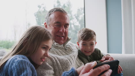 Grandfather-Playing-Video-Game-With-Grandchildren-On-Mobile-Phone-At-Home