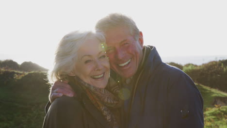 Portrait-Of-Loving-Active-Senior-Couple-Walking-Along-Coastal-Path-Against-Flaring-Sun