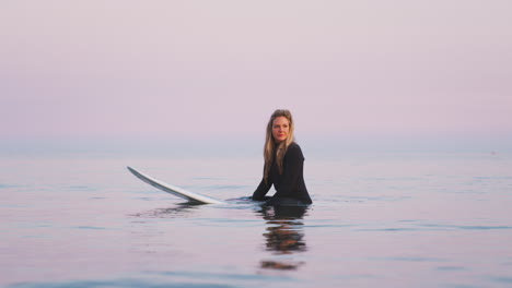 Woman-Wearing-Wetsuit-Sitting-And-Floating-On-Surfboard-At-Sea-As-Waves-Break-Around-Her