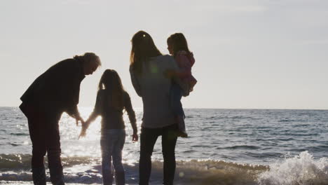 Rear-View-Of-Grandmother-With-Mother-And-Granddaughters-Looking-Out-To-Sea-Silhouetted-Against-Sun