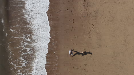 Drone-Shot-Of-Family-On-Vacation-Running-Along-Beach-By-Breaking-Waves