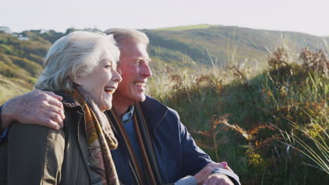 Loving-Active-Senior-Couple-Hugging-As-They-Sit-And-Look-At-Countryside-Together