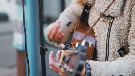 Close-Up-Of-Female-Musician-Busking-Playing-Acoustic-Guitar-Outdoors-In-Street