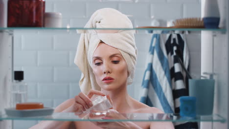 Blick-Durch-Den-Badezimmerschrank-Auf-Eine-Frau,-Die-Ein-Handtuch-Auf-Dem-Kopf-Trägt-Und-Highlighter-Make-up-Aufträgt