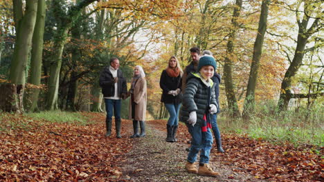 Multi-Generation-Family-Walks-Along-Path-Through-Autumn-Countryside-As-Grandson-Dances-In-Foreground