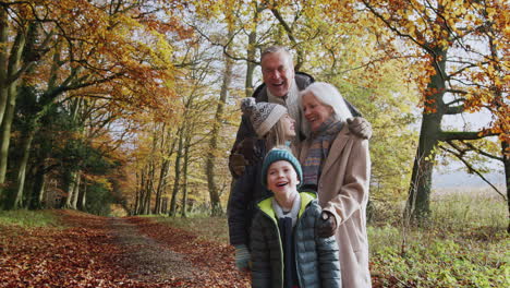 Portrait-Of-Smiling-Grandparents-Walking-With-Grandchildren-Along-Path-In-Autumn-Countryside