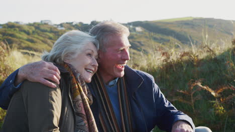 Loving-Active-Senior-Couple-Hugging-As-They-Sit-And-Look-At-Countryside-Together
