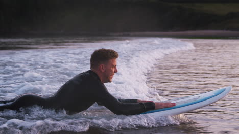 Man-Wearing-Wetsuit-Lying-On-Surfboard-And-Riding-Wave-Into-Shore