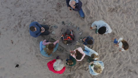Drone-Shot-Of-Multi-Generation-Family-Toasting-Marshmallows-Around-Fire-On-Winter-Beach-Vacation