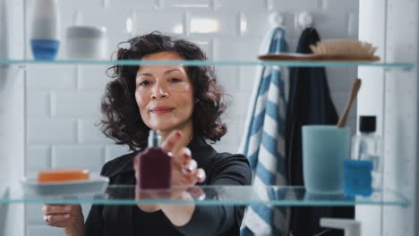 View-Through-Bathroom-Cabinet-Of-Mature-Woman-Spraying-Perfume-From-Bottle