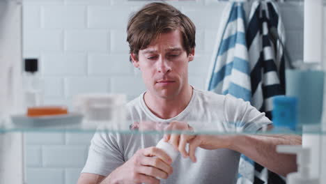 View-Through-Bathroom-Cabinet-Of-Young-Man-Taking-Medication-From-Container