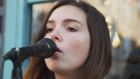 Female-Musician-Busking-Singing-Into-Microphone-Outdoors-In-Street