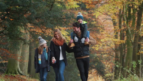 Lächelnde-Familie-Geht-Den-Weg-Durch-Die-Herbstliche-Landschaft-Entlang,-Während-Der-Vater-Seinen-Sohn-Auf-Den-Schultern-Trägt