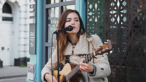 Female-Musician-Busking-Playing-Acoustic-Guitar-And-Singing-Outdoors-In-Street