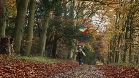 Young-Boy-Having-Fun-Running-Along-Path-Through-Autumn-Countryside-Flying-Kite