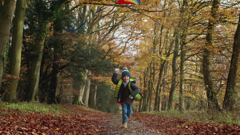 Young-Boy-Having-Fun-Running-Along-Path-Through-Autumn-Countryside-Flying-Kite