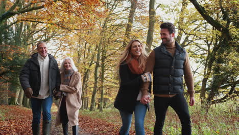 Multi-Generation-Family-Walks-Along-Path-Through-Autumn-Countryside-With-Children-Running-Ahead
