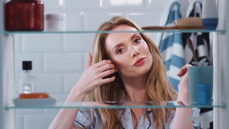 View-Through-Bathroom-Cabinet-Of-Young-Woman-Wearing-Pajamas-Checking-Hair