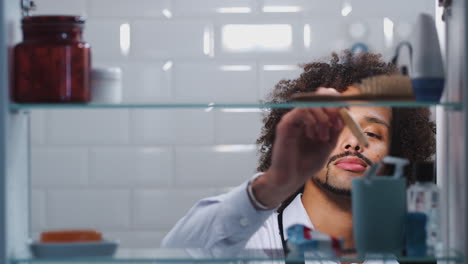 Blick-Durch-Den-Badezimmerschrank-Auf-Einen-Frustrierten-Jungen-Mann,-Dem-Die-Zahnpasta-Für-Die-Zahnbürste-Ausgeht