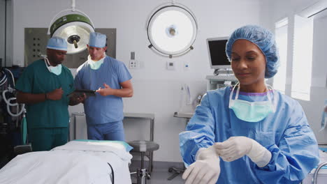 Female-Surgeon-Wearing-Scrubs-Putting-On-Latex-Gloves-In-Hospital-Operating-Theater