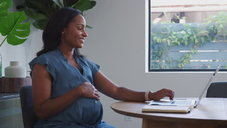 Mujer-Afroamericana-Embarazada-Usando-Una-Computadora-Portátil-En-La-Mesa-Trabajando-Desde-Casa