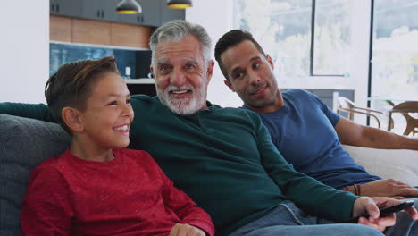 Multi-Generation-Male-Hispanic-Family-Sitting-On-Sofa-At-Home-Watching-Movie-Together