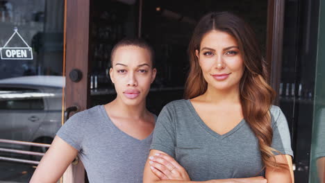 Portrait-Of-Two-Female-Owners-Of-Start-Up-Coffee-Shop-Or-Restaurant-Standing-In-Doorway