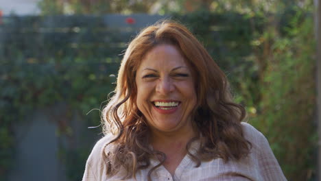 Portrait-Of-Smiling-Senior-Hispanic-Woman--In-Garden-At-Home-Against-Flaring-Sun