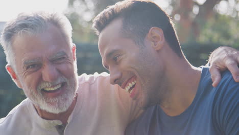 Portrait-Of-Senior-Hispanic-Man-Talking-And-Laughing-With-Adult-Son-In-Garden-At-Home