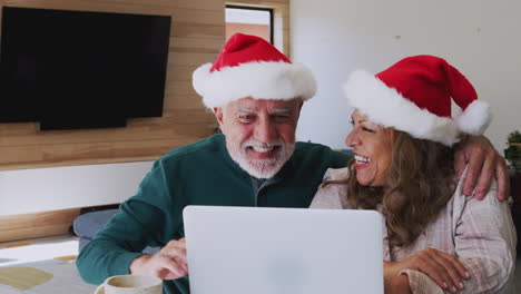 Älteres-Hispanisches-Paar-Mit-Weihnachtsmützen-Und-Laptop,-Das-Zu-Weihnachten-Einen-Videochat-Mit-Der-Familie-Führt