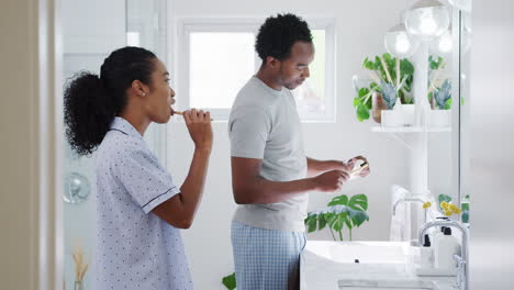 Couple-Wearing-Pyjamas-Standing-In-Bathroom-At-Sink-Brushing-Teeth-In-The-Morning