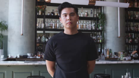 Portrait-Of-Confident-Male-Owner-Of-Restaurant-Bar-Standing-Inside-By-Counter