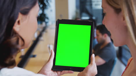 Close-Up-Of-Two-Businesswomen-Looking-At-Blank-Digital-Tablet-With-Green-Screen-In-Shared-Office