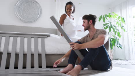 Interracial-Couple-With-Pregnant-Woman-Looking-At-Instructions-For-Self-Assembly-Baby-Cot