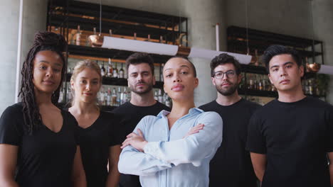 Portrait-Of-Female-Owner-Of-Restaurant-Bar-With-Team-Of-Waiting-Staff-Standing-By-Counter